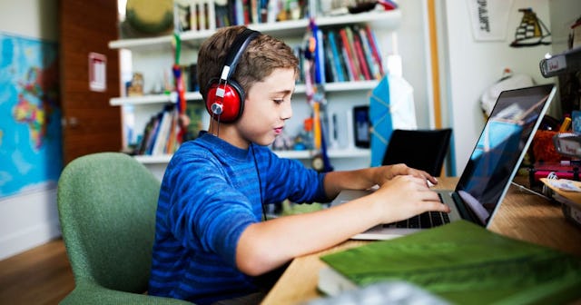 A boy in a blue shirt with headphones chatting online on his laptop