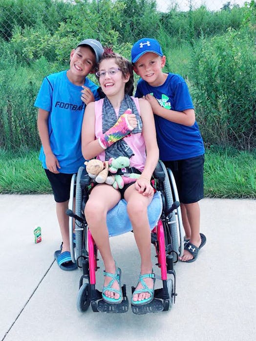 Cara's daughter who got sick in a wheelchair and her two sons standing beside her and smiling