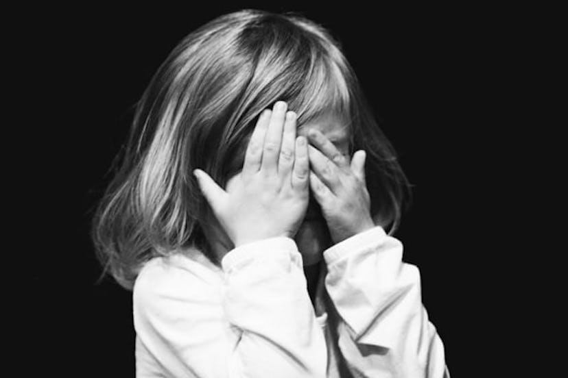 A little girl covering her face with her hands in a black and white photo 