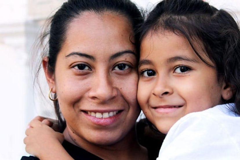 Young mom in a black shirt holding and hugging her little girl in a white shirt