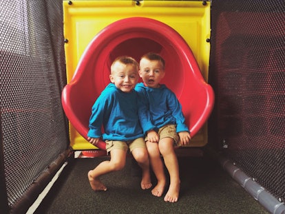 Twin brothers in matching outfits sitting on a slide 