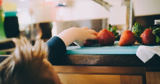 A toddler taking a strawberry from a kitchen counter.