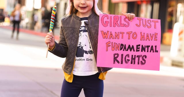 A girl holding a lollipop and a banner saying that 'girls want to have fundamental rights', whose mo...