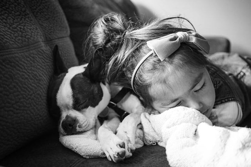 A little girl sleeping next to her dog with a hair bow in black and white