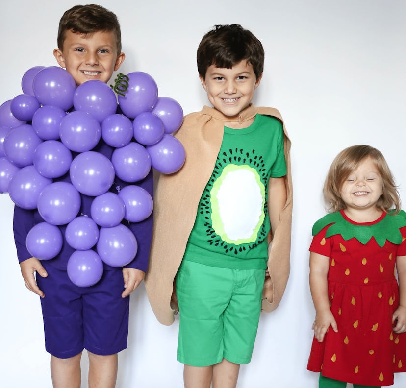 Two boys and a girl posing in grapes, kiwi, and strawberry fruit kids' costumes