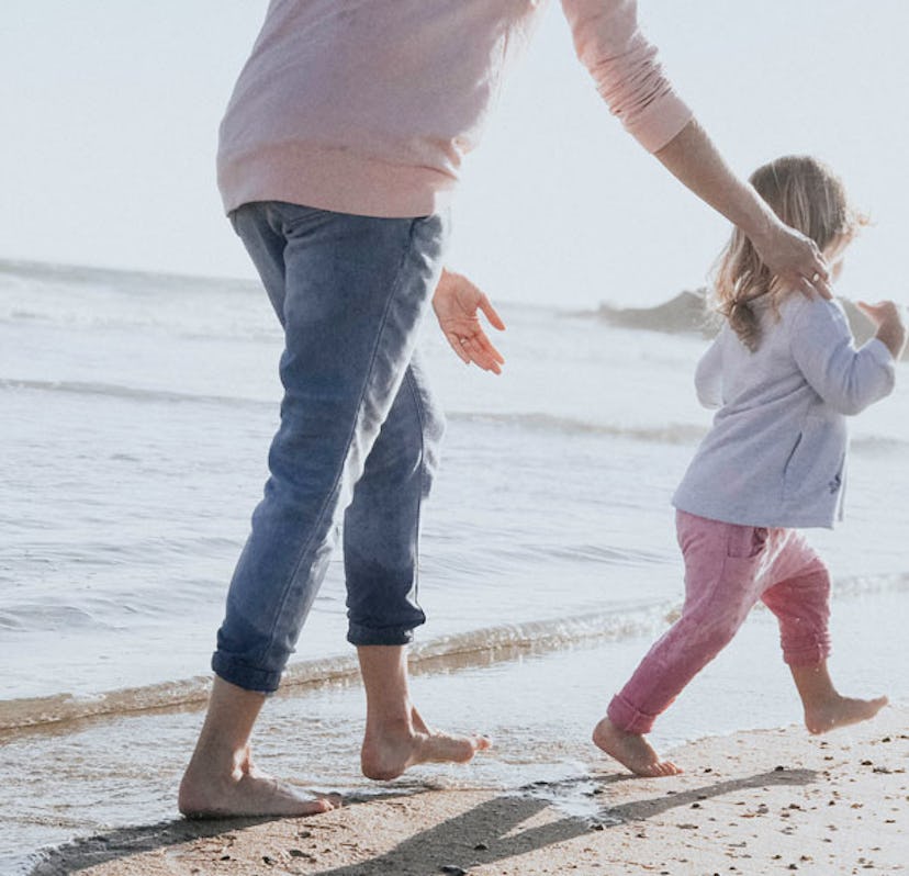 A mother running behind her little stepdaughter at the beach trying to catch her.