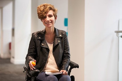 A preteen girl sitting in a wheelchair in a black leather jacket and smiling