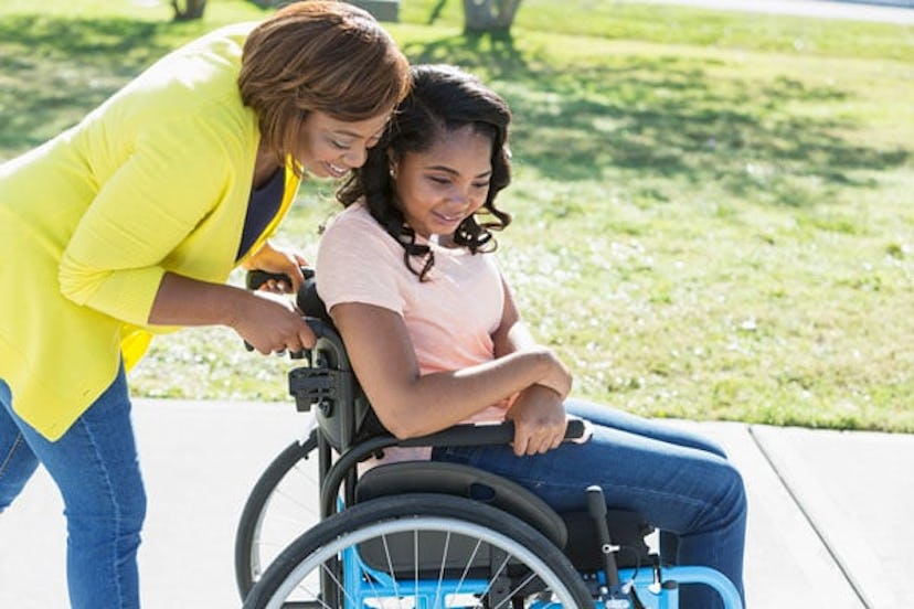 A mother leaning over her preteen daughter in a wheelchair and smiling