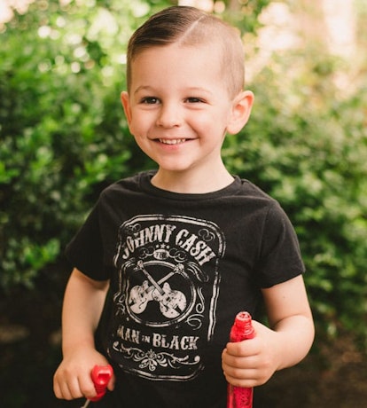 A portrait of Stephanie Hanharan's son standing and smiling while wearing a black Johnny Cash T-Shir...