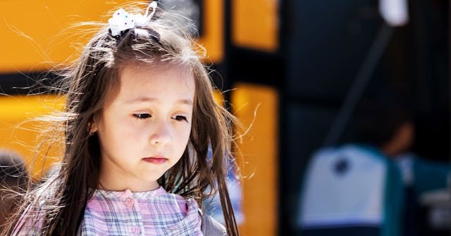 A sad-looking girl who is being bullied walking next to a school bus