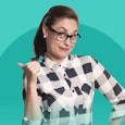 A woman in glasses a ponytail and a plaid button up shirt pointing behind her while looking suggesti...
