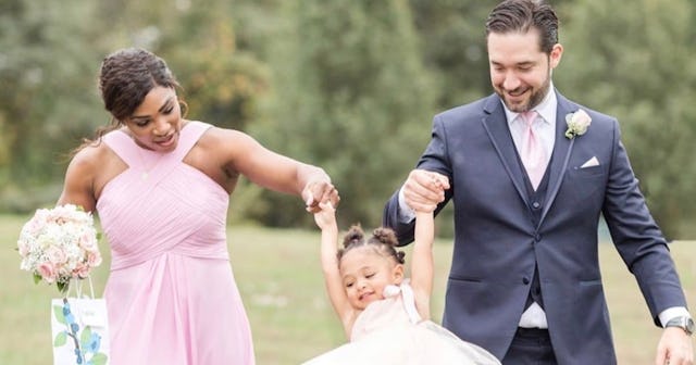 Serena Williams in a pink dress and Alexis Ohanian in a navy suit with their flower girl daughter