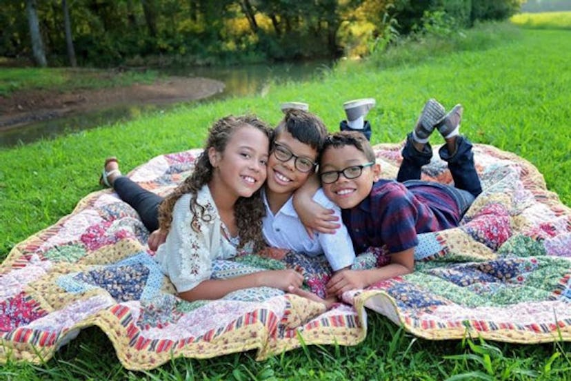 Joanna Yates's children are laying together and hugging each other on a blanket in a park.