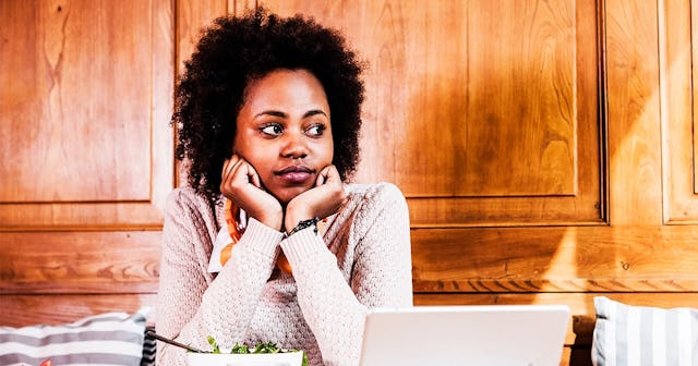 A mom with an eating disorder supporting her head with her arms, sitting in front of a salad and a l...