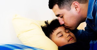 A father putting his son to bed and kissing him on the forehead before bedtime
