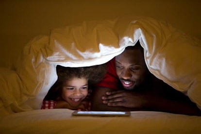 Father and son in bed under a duvet watching videos on the tablet before bedtime