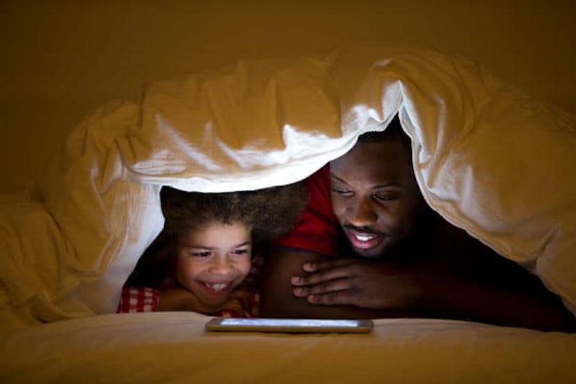 Father and son in bed under a duvet watching videos on the tablet before bedtime