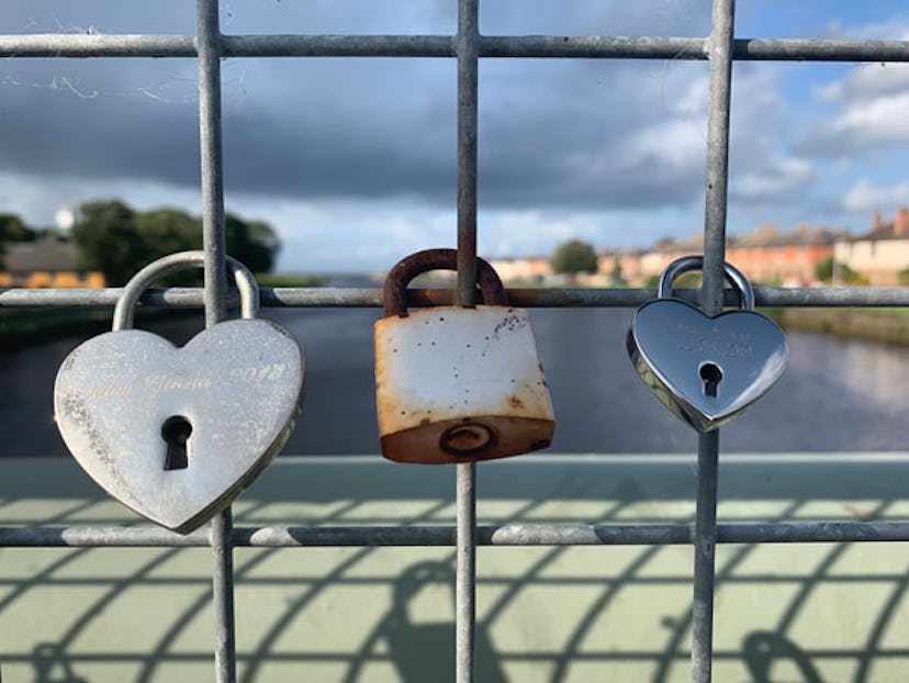 A rusty lock in the middle of two silver heart-shaped locks on a bridge fence