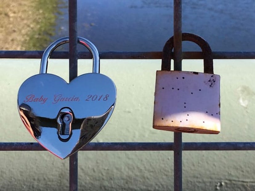 A silver heart-shaped lock from 2018 and a pink rusty lock on a bridge fence