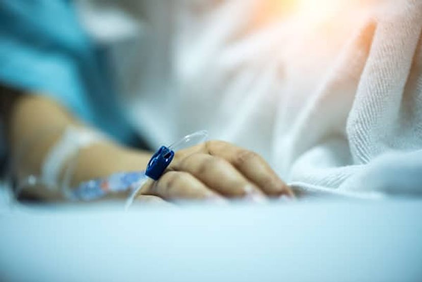 A close-up of a person's hand in a hospital bed with a cannula attached to it