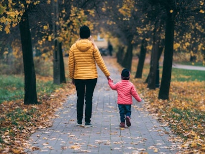 A mom and her daughter in winter jackets walking through the park and holding hands.