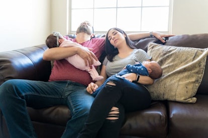 Parents sleeping while sitting on a couch and holding their babies