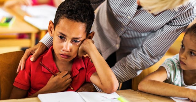 A Teacher Consoling A Sad Boy At His Desk