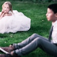 A girl in a white dress and a boy in a suit sitting on the grass  who are indoctrinated to the cisge...