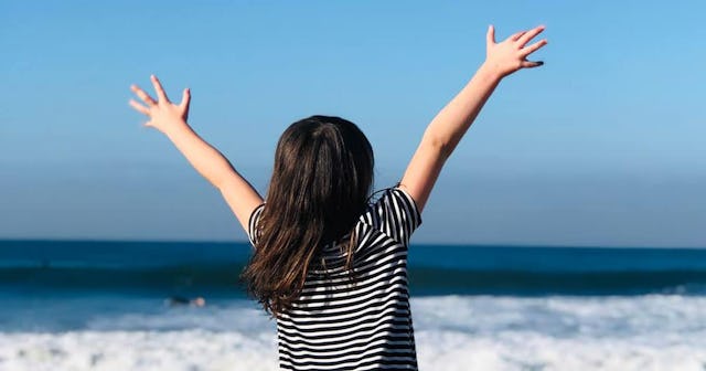A tween girl with autism with raised arms looking at a sea