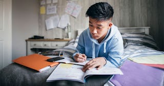 A teenage boy in a light blue hoodie, studying in his bedroom