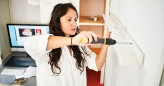 A single mom setting up a shelf on the wall by following instructions on YouTube displayed on a PC m...