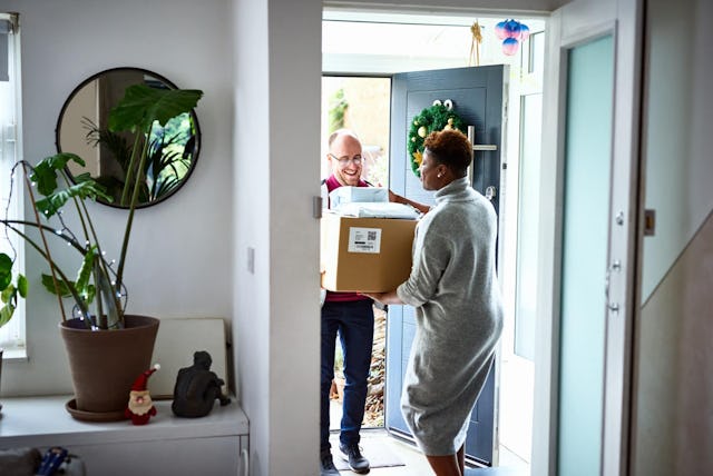 Woman receiving delivery from courier at front door, Christmas wreath, Christmas shopping, convenien...