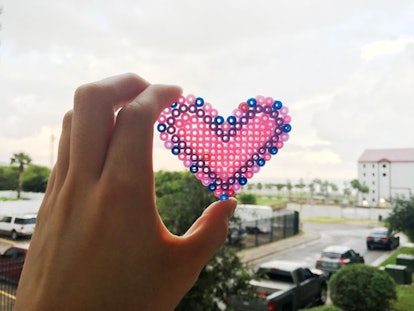 A hand holding a crafted pink and blue heart against the skyline