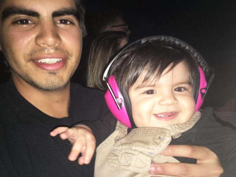 Maxwell and his dad at a rock concert. Maxwell is in his dad's arms, wearing pink infant earmuffs an...