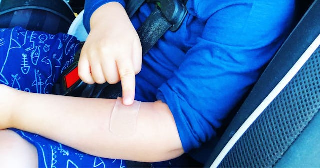 A small boy sitting in a car with a band-aid on his left arm covering a bite mark