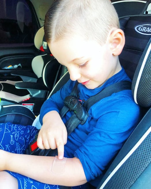A small boy sitting in a car with a band-aid on his left arm covering a bite mark