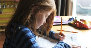 A girl in a blue-striped long-sleeved shirt sitting and doing her homework on a wooden table