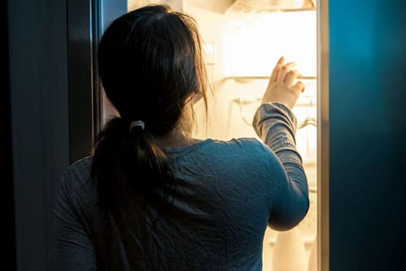 A gril who is sleepwalking opening a fridge in the middle of the night