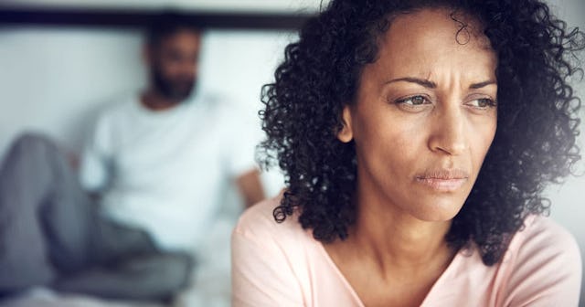 A woman wearing a pink shirt with an angry look on her face, with a blurred ex-husband in the backgr...
