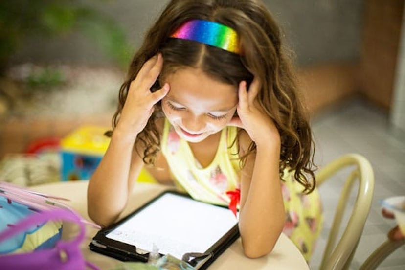 Little girl sitting at a desk while watching something at her tablet