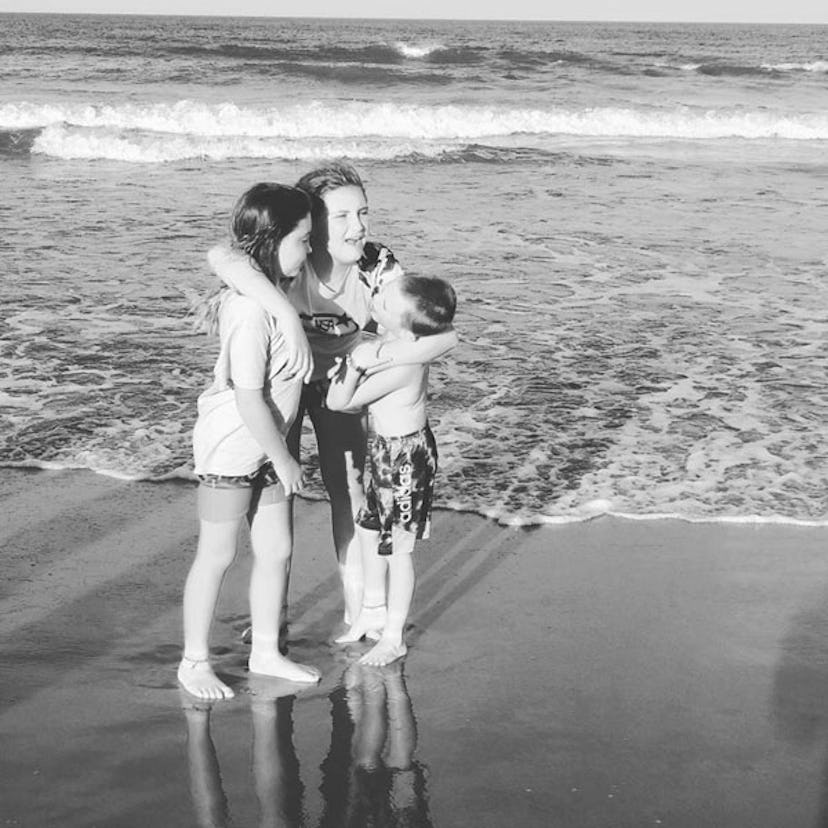 Three kids hugging next to sea on a sand beach
