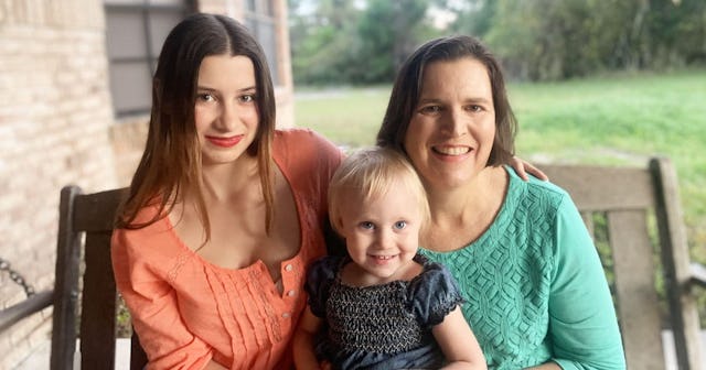 Julie Raeburn sitting on a bench next to her teen daughter, while holding her two-year-old child.