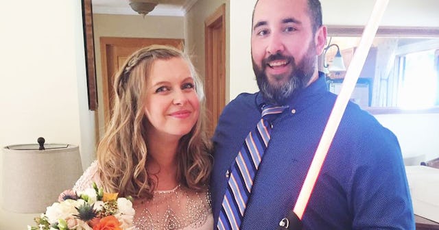 Man and woman standing next to each other whilst he is holding a lightsaber.