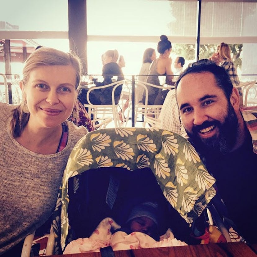 A selfie of woman and man with their kid in the stroller which is covered by a blanket.