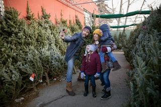 Happy family taking selfie, shopping for Christmas tree at Christmas market