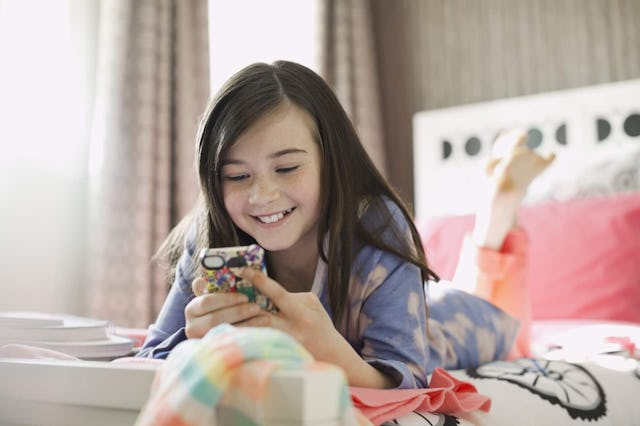 Smiling girl using smart phone in bed