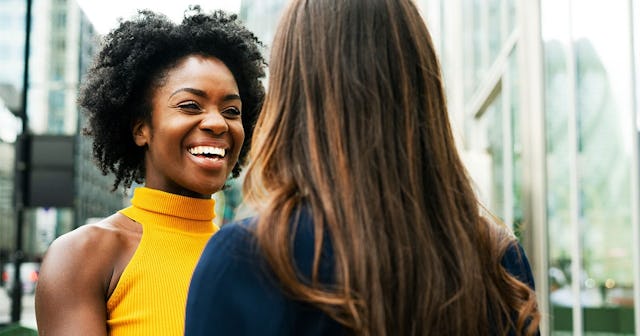 A woman in a yellow knit sleeveless turtleneck bragging about her kid to her friend