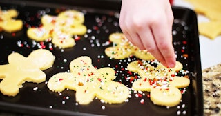 A kid putting sprinkles on a sugar cookie on a black tray