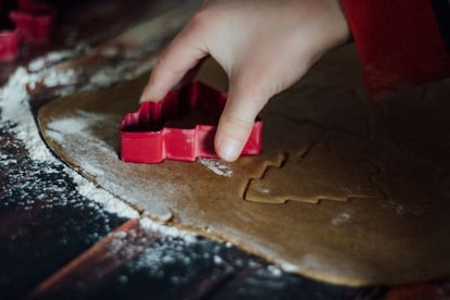 A kid is cutting out sugar cookies from dough with a Christmas tree tool