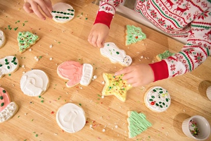 A kid putting sprinkles on Christmas-themed sugar cookies on a wooden surface